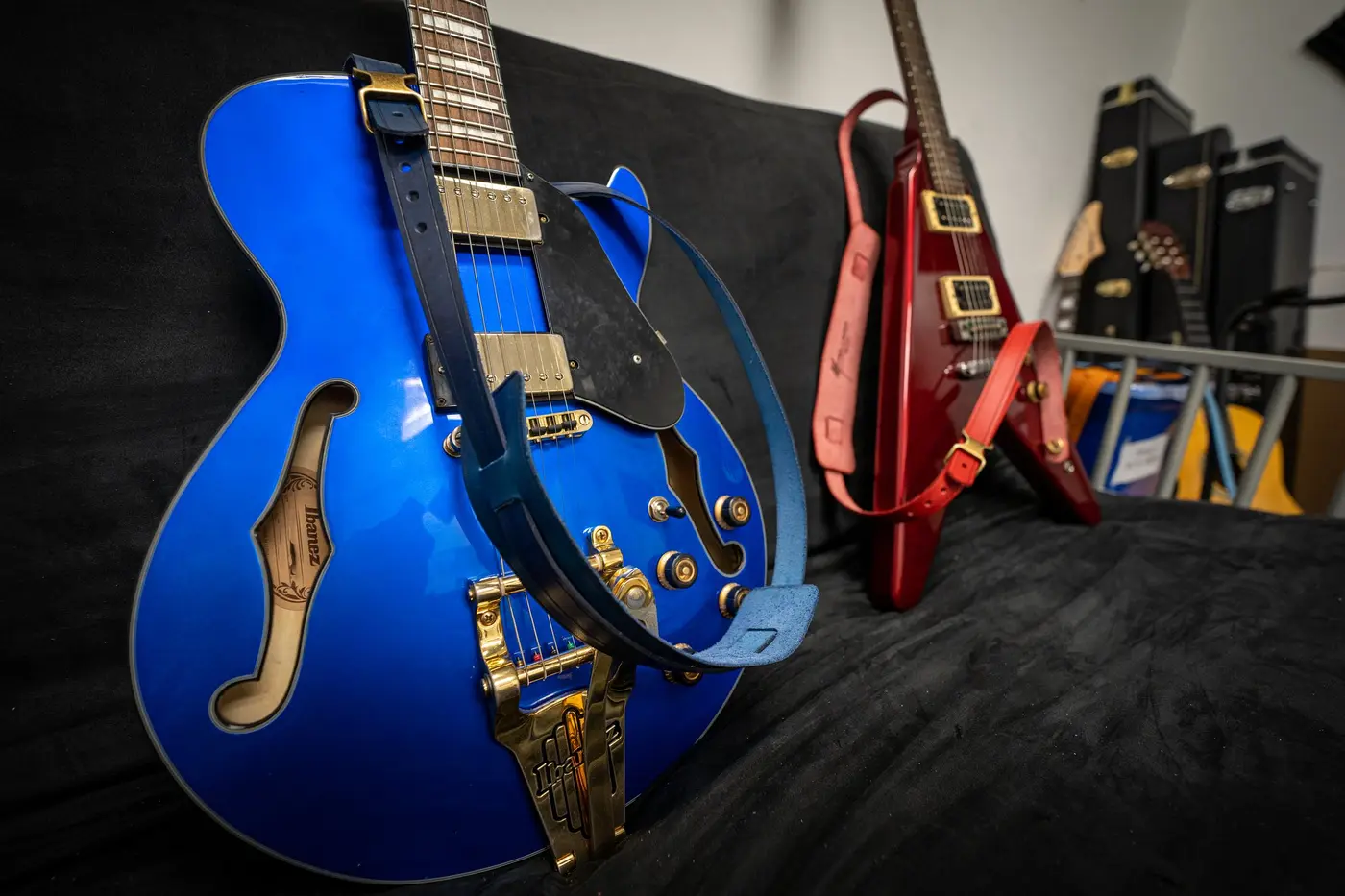 A blue hollow-body guitar and a red Flying V, each wearing a handmade leather strap, on a black couch