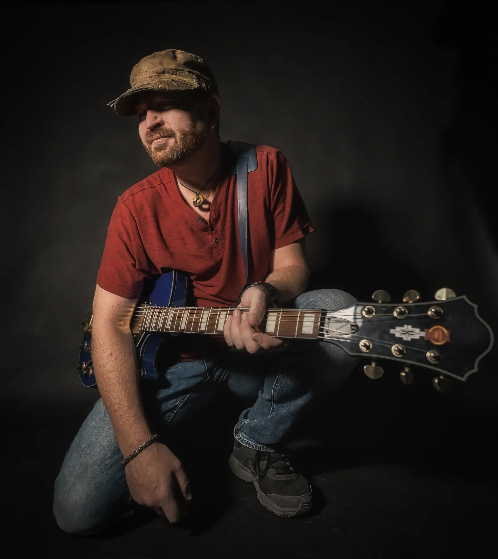 Michael Lander crouching with an electric guitar against a dark backdrop