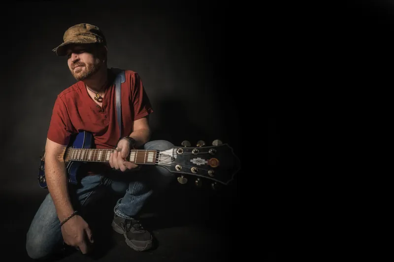 Michael Lander: Portrait kneeling with electric guitar, red shirt